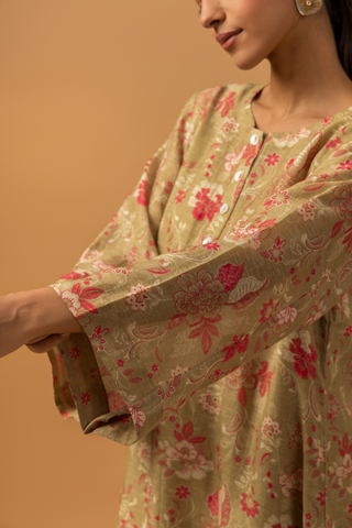 Closeup view of a woman showing her hand and wearing a floral-patterned co-ord set with matching pants stands against a tan background, conveying a calm and elegant tone.