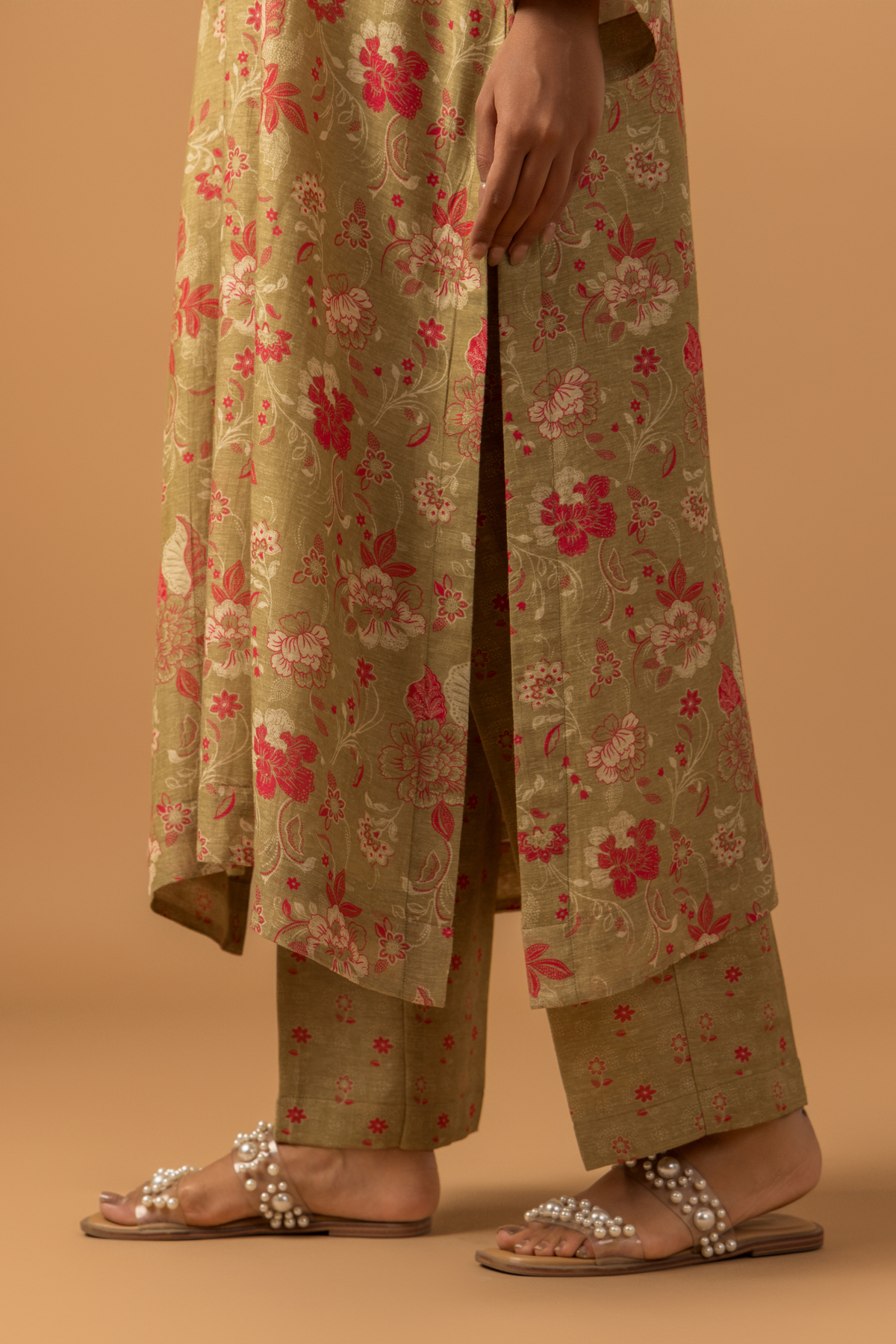 Closeup view of a woman in floral-patterned co-ord set with matching pants stands against a tan background, conveying a calm and elegant tone.