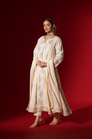 Side view of a woman showcases an elegant white anarkali kurta set with intricate designs, contrasting beautifully against a deep red background.