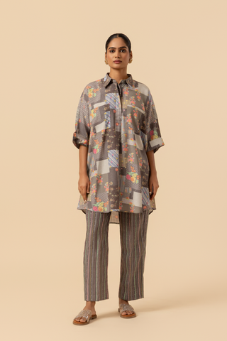 A woman wearing a floral patterned oversized shirt and striped pants, standing against a neutral background.