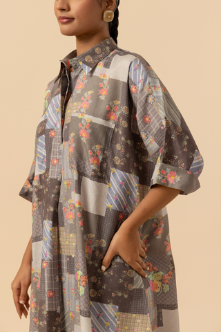 A model displays a stylish, oversized, patchwork shirt with floral and geometric patterns, set against a soft beige background.