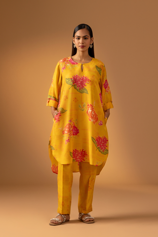 A woman in a vibrant yellow floral co-ord set and matching pants stands confidently against a warm, neutral background.