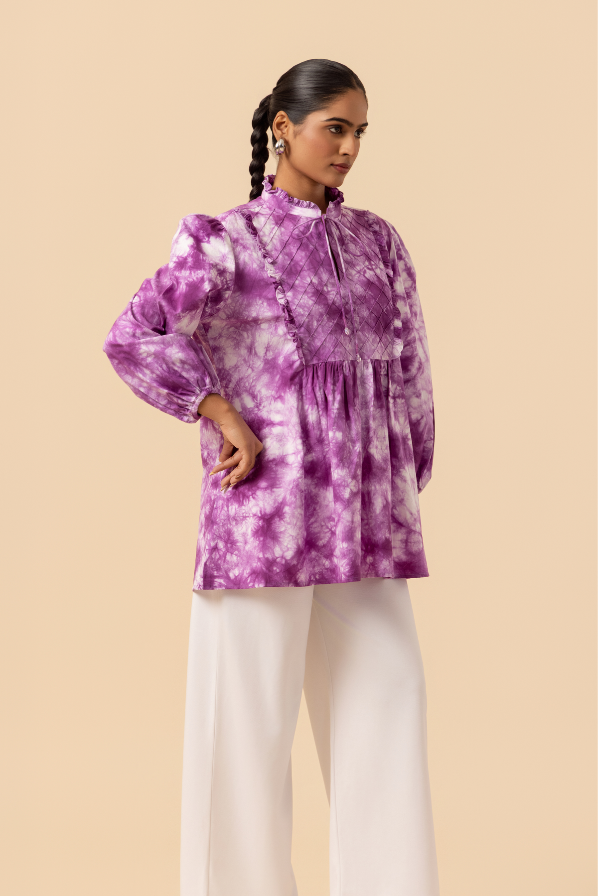 Right side view of a model wears a vibrant purple tie-dye shirt dress with puffed sleeves, paired with white wide-leg trousers and stylish sandals.