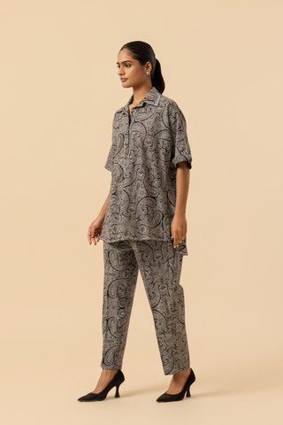 Side view of a person stands confidently in a matching patterned outfit, featuring a loose shirt and tailored pants, paired with stylish heels.