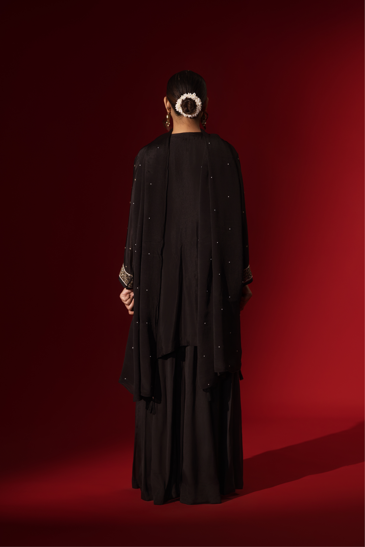 Back view of a woman showcases an elegant black embroidered kurta set with intricate gold embroidery against a rich red backdrop.