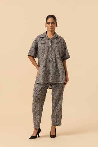 A person stands confidently in a matching patterned outfit, featuring a loose shirt and tailored pants, paired with stylish heels.