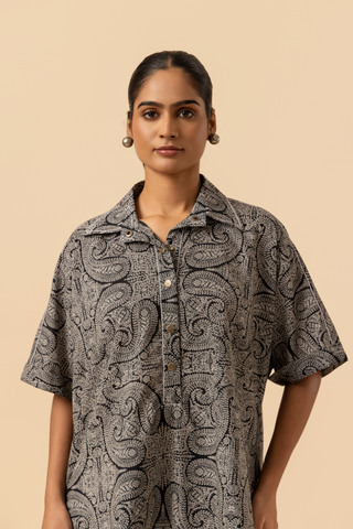 Closeup view of a person stands confidently in a matching patterned outfit, featuring a loose shirt and tailored pants, paired with stylish heels.
