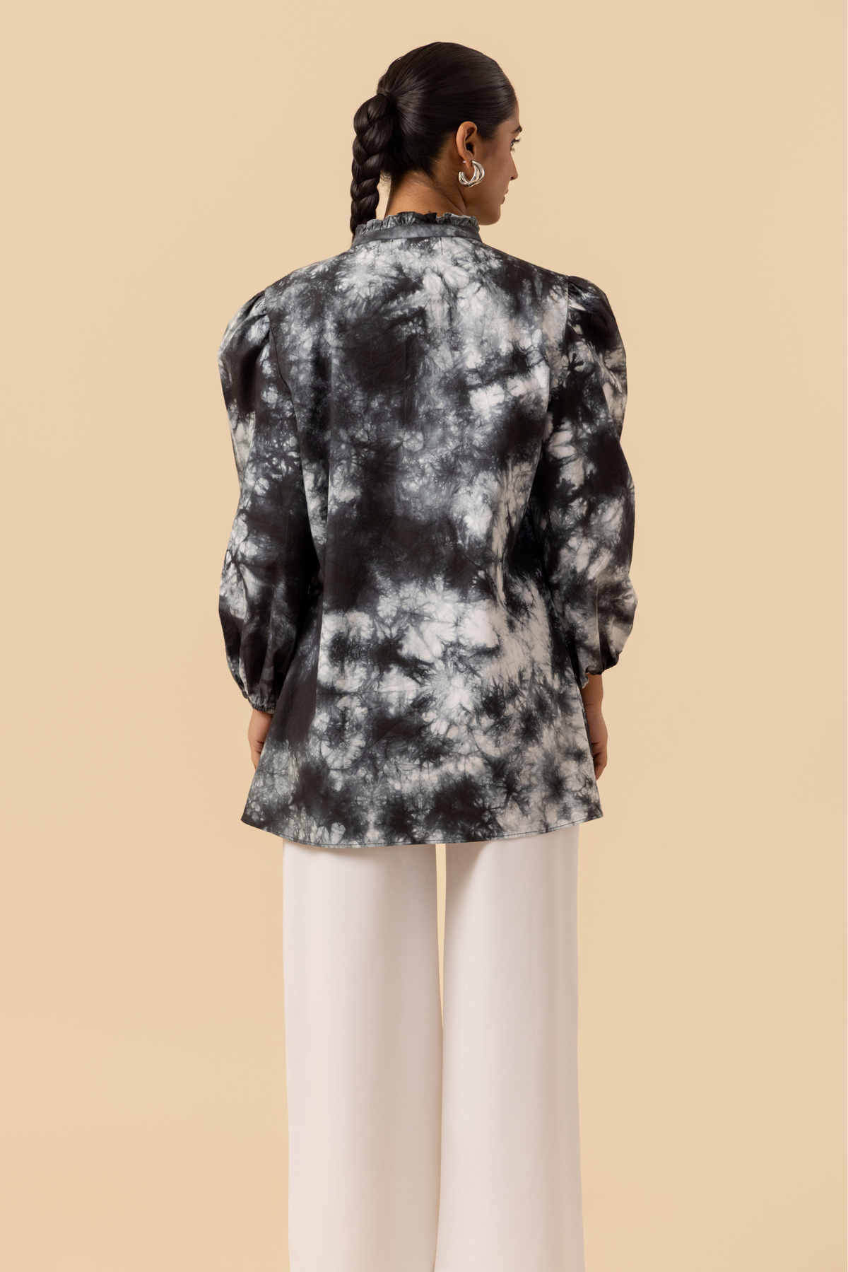 Back side view of a model wears a vibrant black & white tie-dye shirt dress with puffed sleeves, paired with white wide-leg trousers and stylish sandals.