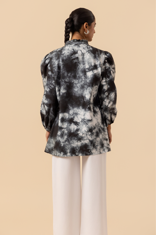 Back side view of a model wears a vibrant black & white tie-dye shirt dress with puffed sleeves, paired with white wide-leg trousers and stylish sandals.