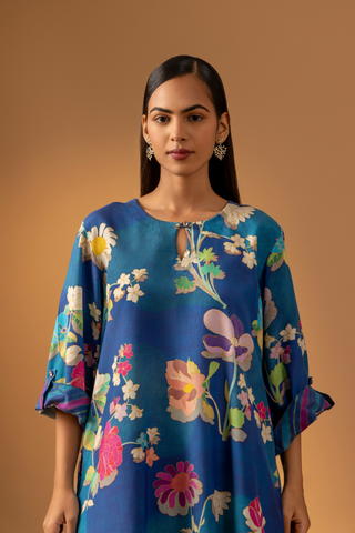 Closeup view of a woman models a vibrant floral co-ord set paired with striped pants, set against a warm, neutral background.