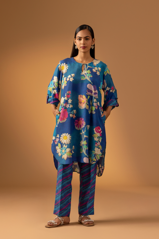 A woman models a vibrant floral co-ord set paired with striped pants, set against a warm, neutral background.