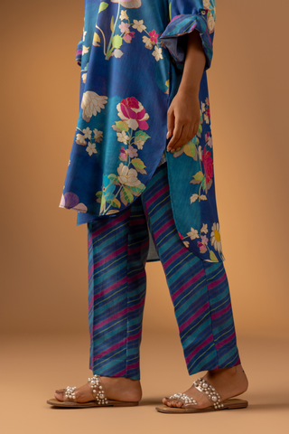 A close-up of a woman woman models a vibrant floral co-ord set paired with striped pants, set against a warm, neutral background.