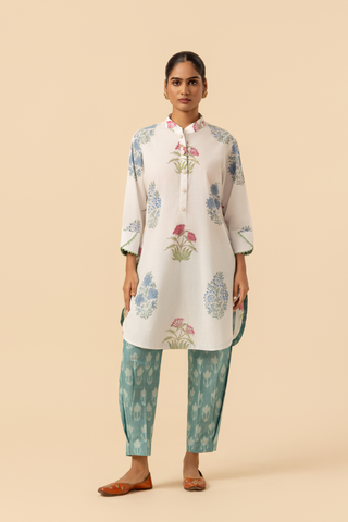 A woman stands wearing a floral-printed tunic and teal pants cotton co-ord set, set against a soft beige background, showcasing a stylish ethnic outfit.