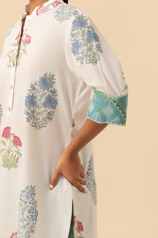 A model stands wearing a floral-printed tunic and teal pants cotton co-ord set, set against a soft beige background.