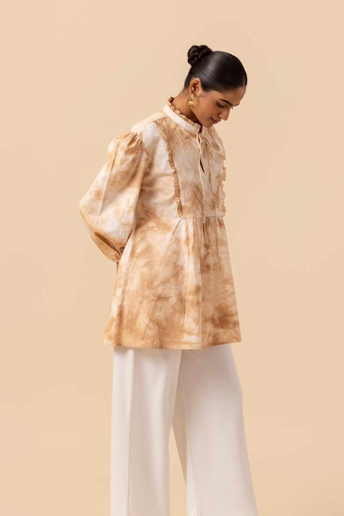 Right side view of a woman wears a vibrant caramel tie-dye shirt dress with puffed sleeves, paired with white wide-leg trousers and stylish sandals.