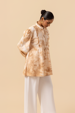 Right side view of a woman wears a vibrant caramel tie-dye shirt dress with puffed sleeves, paired with white wide-leg trousers and stylish sandals.