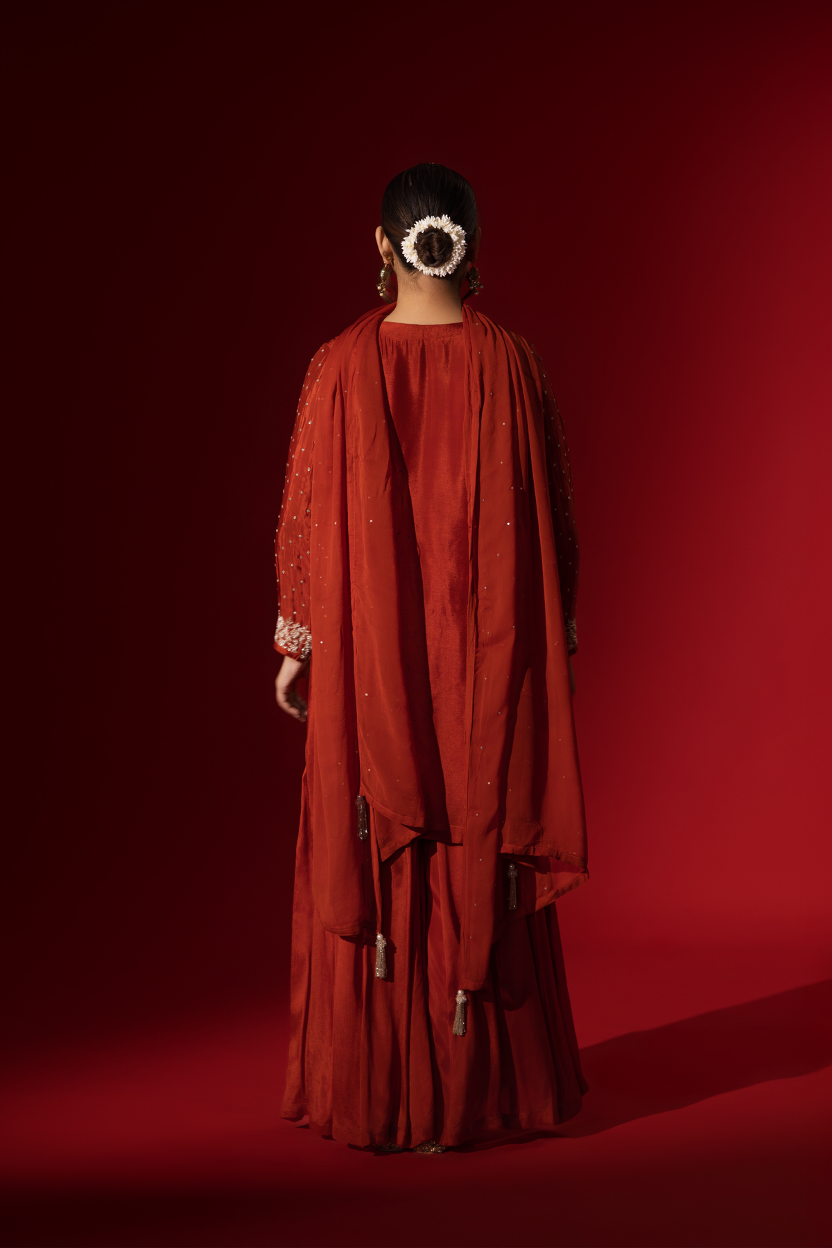 Back view of a woman poses in an elegant red embroidered kurta set adorned with intricate white embroidery against a rich red background.