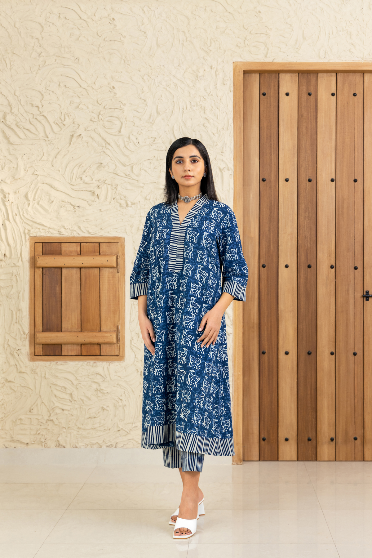Woman wearing a blue and white deer printed co-ord set with striped detailing, standing against a wooden and textured beige background.