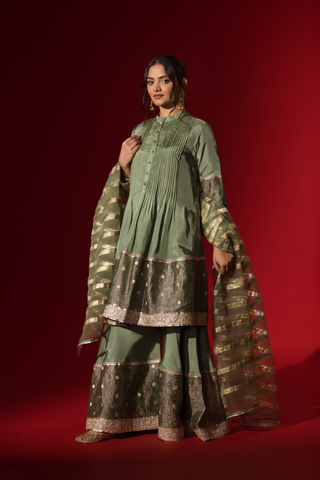 Side view of a model showcasing an elegant green gharara set with gold accents, set against a striking red background.