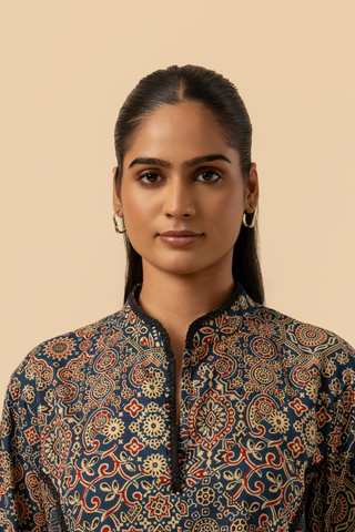 Closeup view of a model wearing a long, patterned ajrakh print co-ord set which has tunic and loose pants, showcasing intricate designs in dark blues and golds against a neutral background.