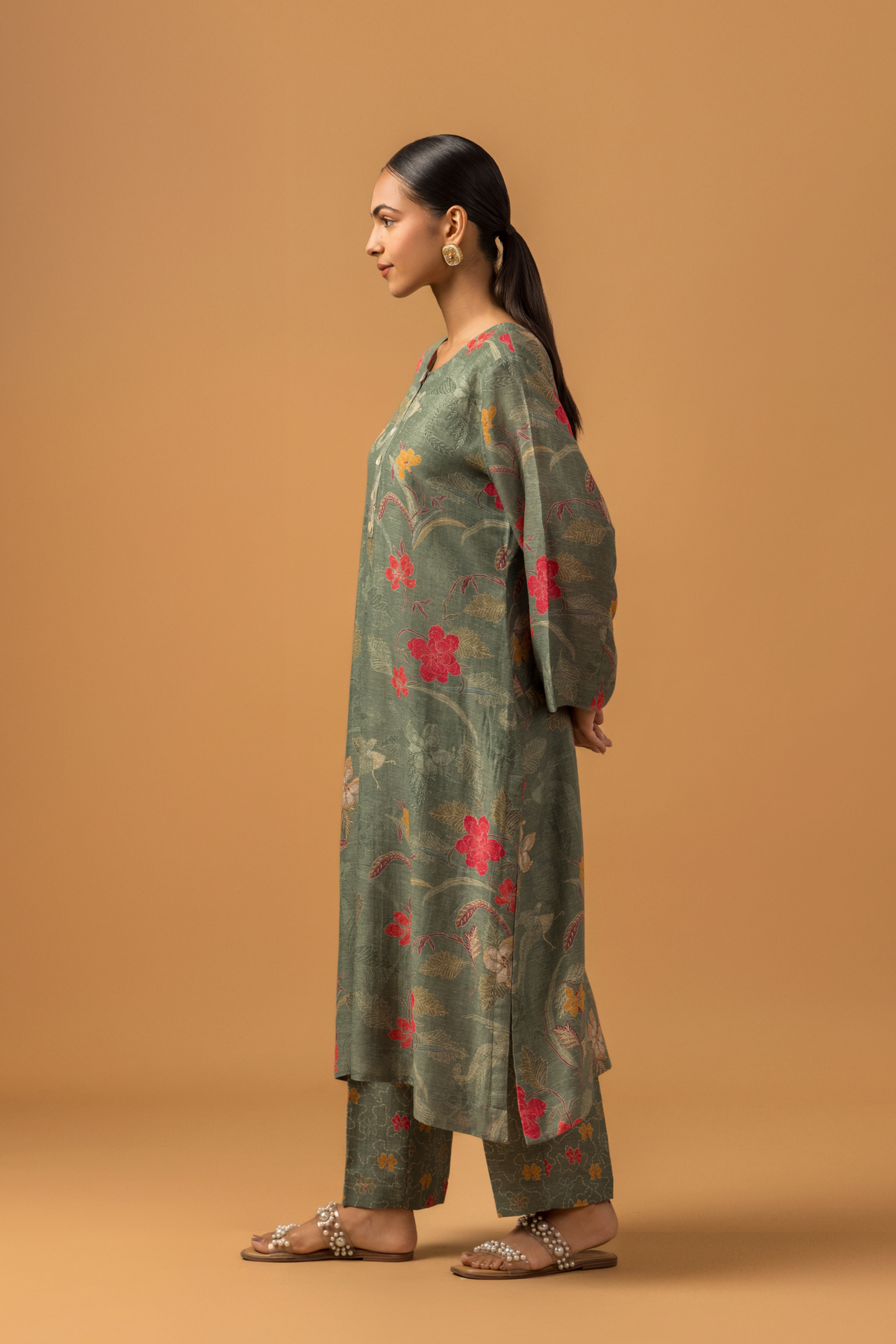 Side view of a woman wearing a dusty green floral line co-ord set and matching pants, set against a warm, neutral background.