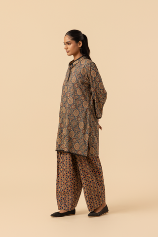 Side view of a model stands in a patterned ajrakh print co-ord set which has brown kurta and matching loose pants against a soft beige background, showcasing traditional ethnic wear.