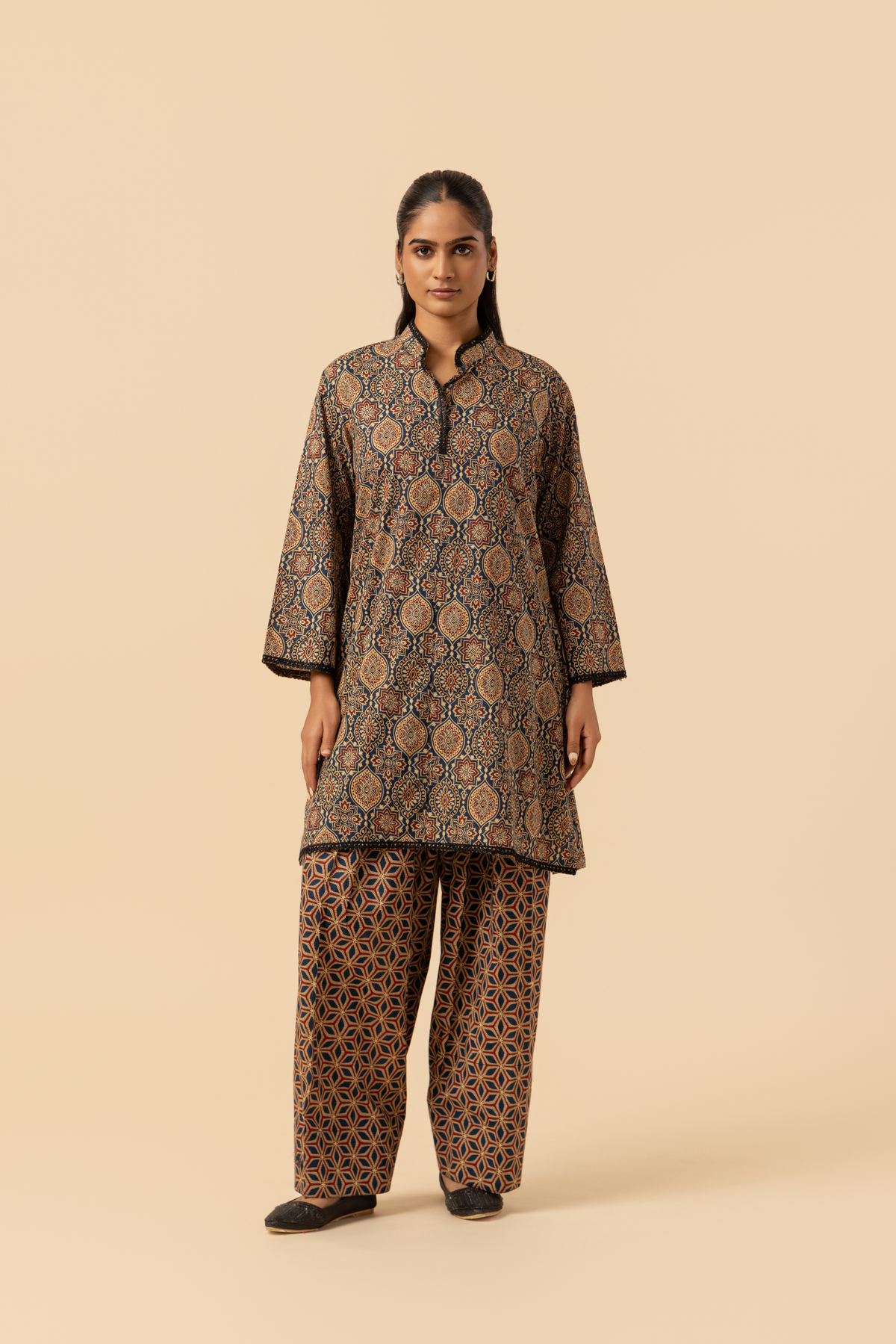 A model stands in a patterned ajrakh print co-ord set which has brown kurta and matching loose pants against a soft beige background, showcasing traditional ethnic wear.