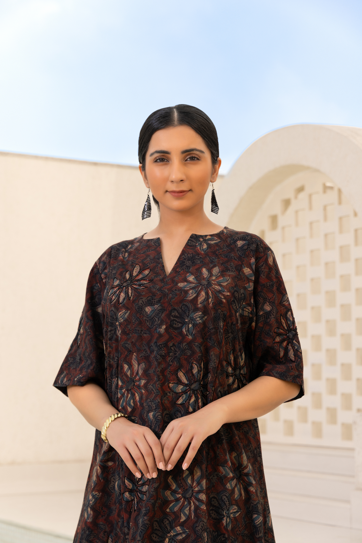 Closeup view of a model dressed in a brown printed kurta set with flower intricate patterns, paired with striped trousers, styled in a serene outdoor setting
