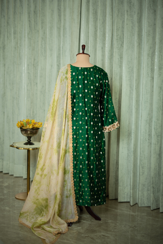 Back view of  a green silk brocade kurta set adorned with golden embroidery, paired with a light, patterned dupatta, displayed on a mannequin.