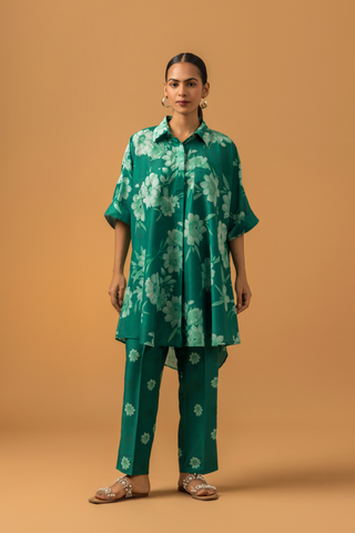 A model poses in a vibrant green floral co-ord set, featuring a loose shirt and matching pants, complemented by embellished sandals.