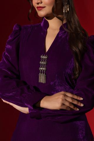 Closeup view of a woman's hand in a vibrant purple velvet co-ord set with a feminine silhouette and elegant earrings, set against a rich red background.