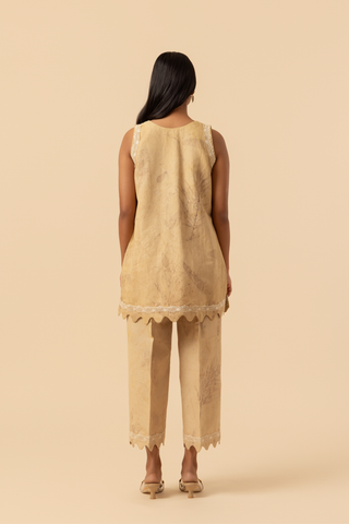 Back view of a person stands in a light beige outfit featuring a sleeveless top and matching pants, complemented by delicate lace detailing.