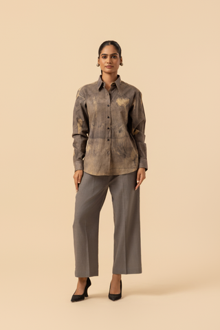 A model stands against a light beige background, wearing a patterned grey co-ord set which has button-up shirt and wide-legged beige pants, accessorized with heels.