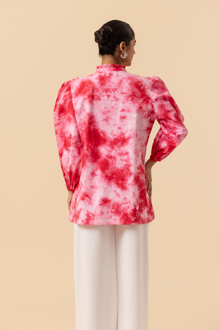 Back side view of a model wears a vibrant cherry red tie-dye shirt dress with puffed sleeves, paired with white wide-leg trousers and stylish sandals.