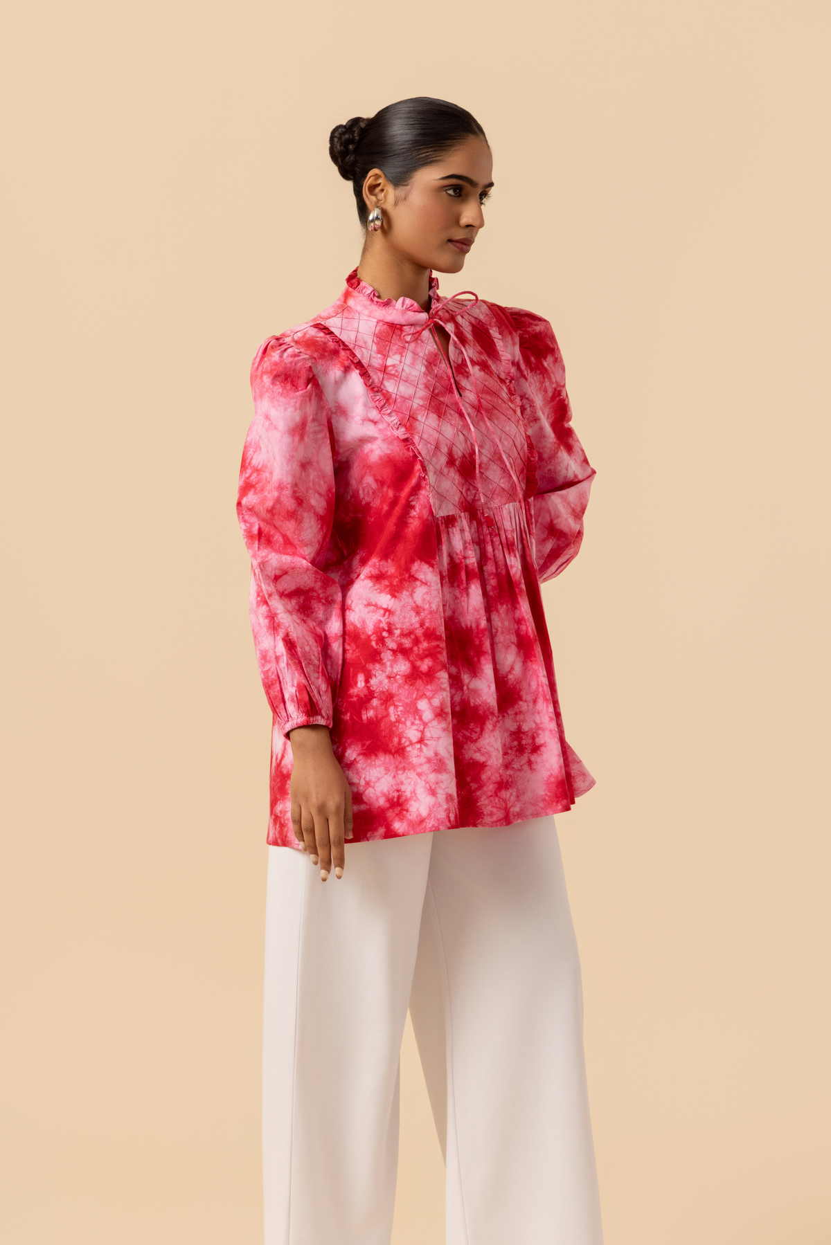 Right side view of a model wears a vibrant cherry red tie-dye shirt dress with puffed sleeves, paired with white wide-leg trousers and stylish sandals.