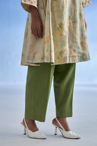 A model is shown from the waist down wearing a beige embroidered linen kurta set, olive green cropped trousers, and white slingback kitten heels against a light blue studio background.