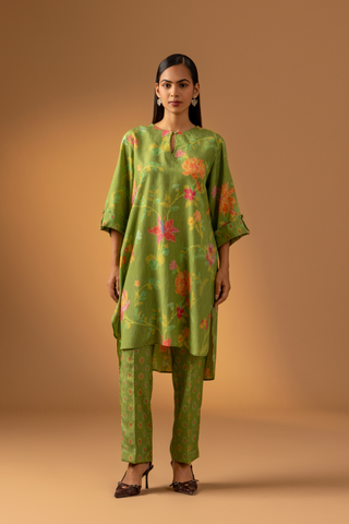 A model stands in a vibrant green co-ord set with floral patterns, paired with matching trousers, against a warm beige background.