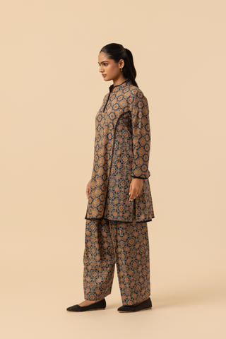 Side view of a woman wearing a patterned ajrakh print farshi co-ord set which has tunic with matching trousers, showcasing vibrant colors and intricate designs against a simple beige background.