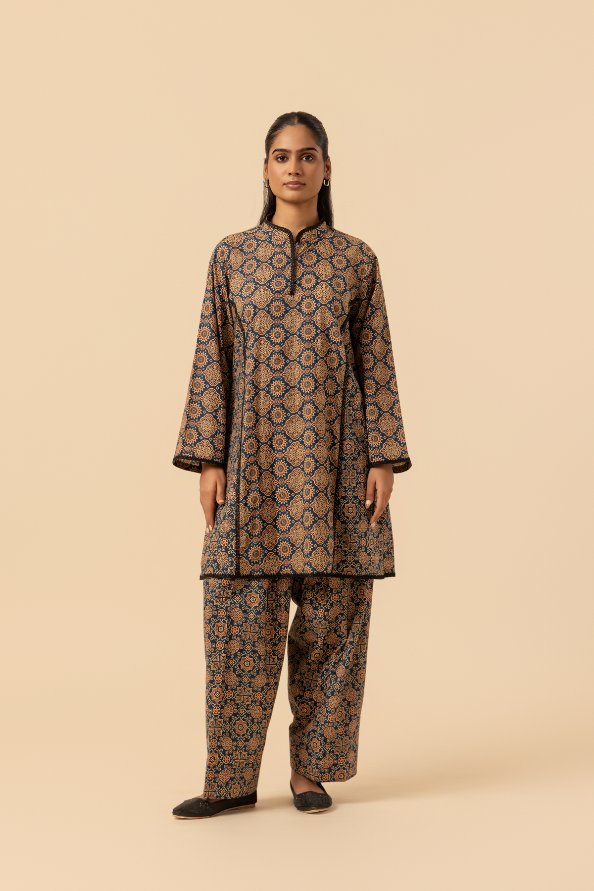 A woman wearing a patterned ajrakh print farshi co-ord set which has tunic with matching trousers, showcasing vibrant colors and intricate designs against a simple beige background.