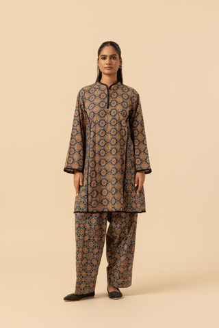 A woman wearing a patterned ajrakh print farshi co-ord set which has tunic with matching trousers, showcasing vibrant colors and intricate designs against a simple beige background.
