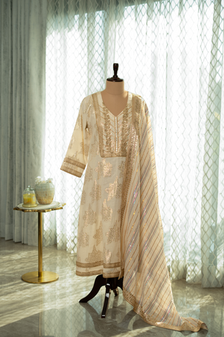 Elegant cream cotton kurta set outfit on a mannequin, featuring intricate gold embroidery and a matching dupatta, set against soft, natural light.