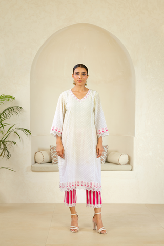 Model showcasing a white handcrafted kurta with pink embroidery and lace details, paired with striped pink pants, exuding elegance and charm