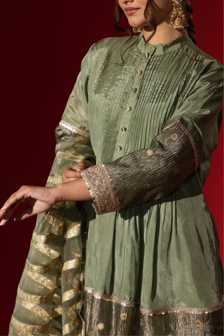 Closeup of a woman's hand showcasing an elegant green gharara set with gold accents, set against a striking red background.