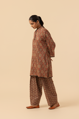 Side view of a model showcases a patterned brown ajrakh print co-ord set and against a beige background, emphasizing traditional ethnic wear.