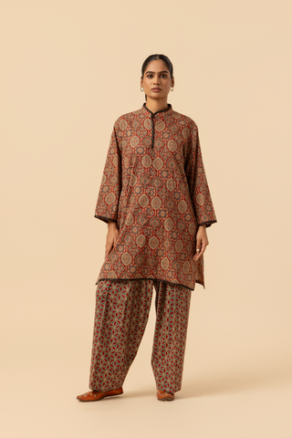 A model showcases a patterned brown ajrakh print co-ord set and against a beige background, emphasizing traditional ethnic wear.