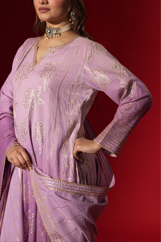 Closeup view of a woman's hand in an elegant lilac anarkali kurta set with intricate designs, contrasting beautifully against a deep red background.