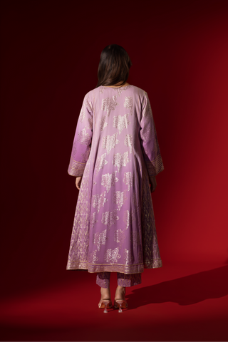 Back view of a woman showcases an elegant lilac anarkali kurta set with intricate designs, contrasting beautifully against a deep red background.