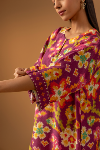 Closeup view of a model showing her hand in a magenta floral-patterned co-ord set paired with colorful striped pants against a warm, neutral background.