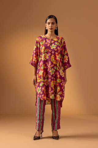 A model showcases a magenta floral-patterned co-ord set paired with colorful striped pants against a warm, neutral background.