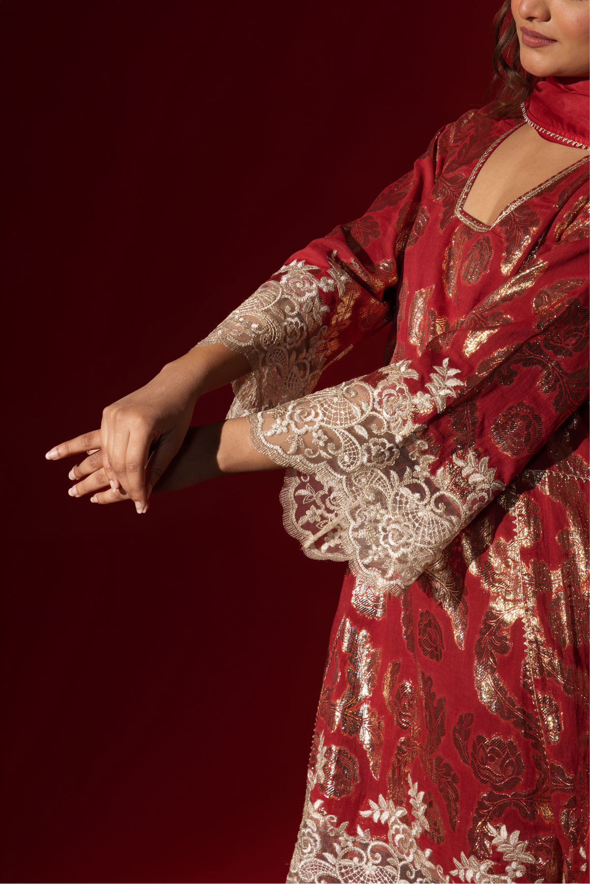 Closeup view of a woman's hand in a maroon ethnic  shimmer kurta set outfit with intricate white embroidery against a vibrant red backdrop.